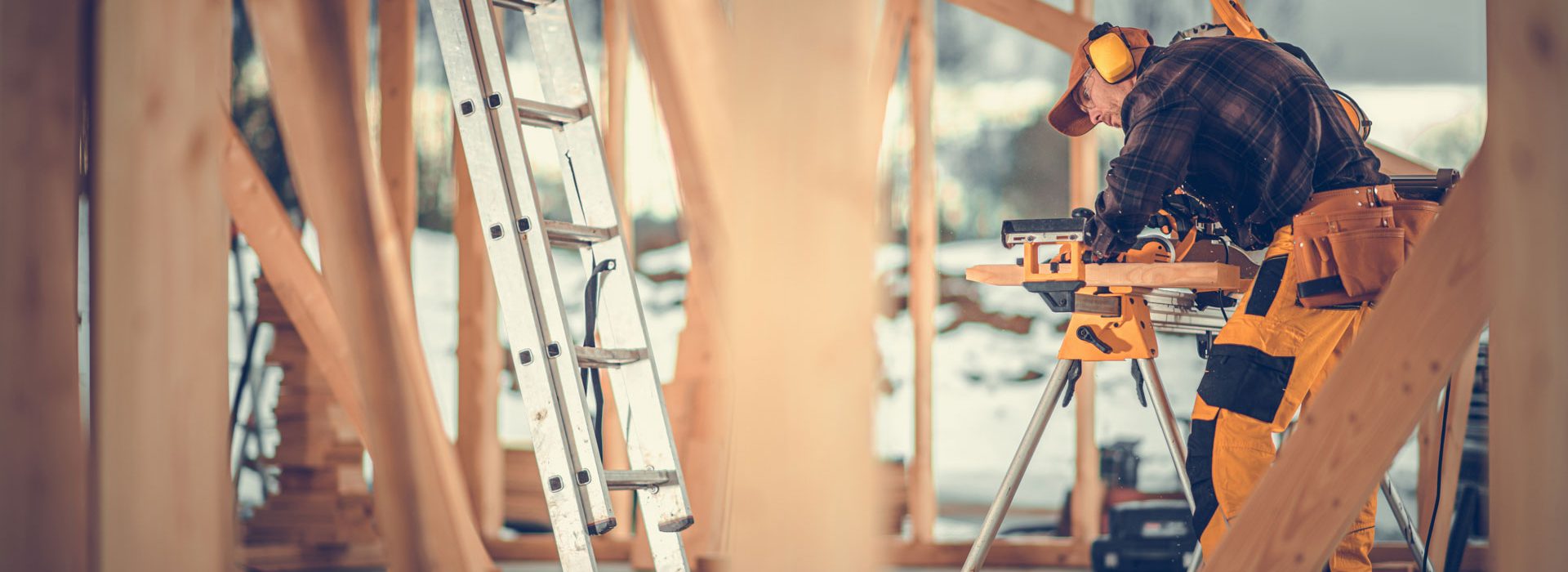 Caucasian Contractor Worker in His 40s Trimming Wooden Elements Using Commercial Grade Powerful Electric Saw. Wooden House Frame Assembly Construction Zone Theme